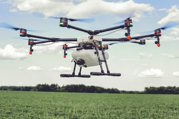 Fototapeta na wymiar Professional agriculture drone flying and green wheat field, Hovering drone flies in blue sky and taking pictures of green hills.