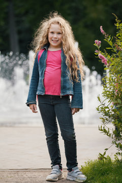 Little blonde smiling child wearing jeans jacket in park