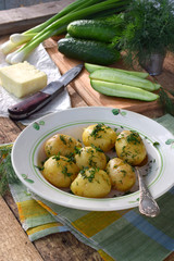 Organically grown new potatoes with butter and dill on wooden background. First spring harvest