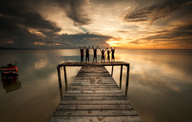 Obraz premium wooden Jetty during sunset with kids silheoutte. Image contain soft focus dule to long exposure.