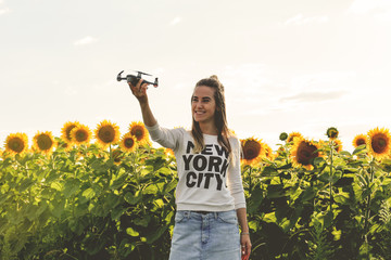 Beautiful woman is holding a mini dron on the background of a field sunflowers. Dron is preparing to take off.