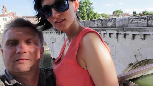 Couple making mobile photo of Tiberius bridge landmark Rimini Italy. Kiss
