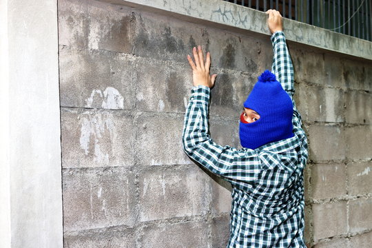 Masked burglar climbs through a fence. Catch burglar concept