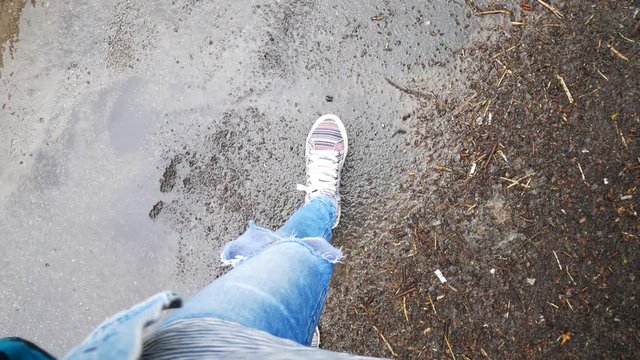 The girl steps on the wet asphalt. In the frame, only female feet in sneakers.