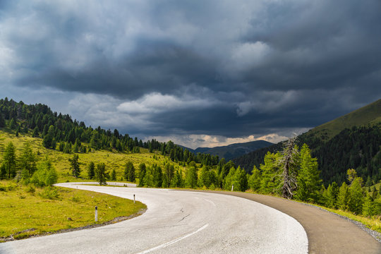 kurvenreiche Straße in den Alpen mit Gewitterwolken 
