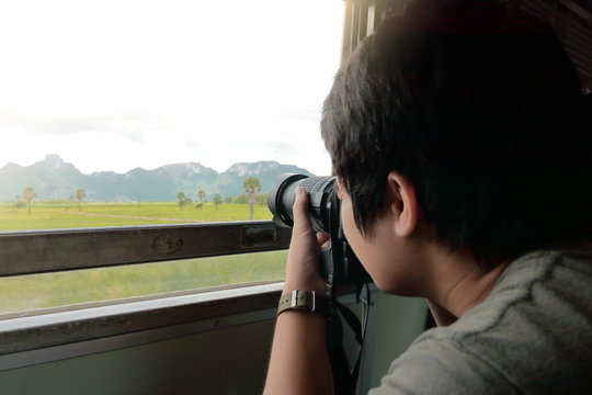 Wide angle shot of young Asian tourist taking a photo of  scenic nature mountain with professional camera in the train