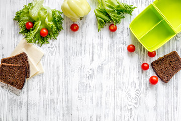 Healthy dinner in office. Lunch box with bread, tomato, salad and cheese on light wooden background top view copyspace