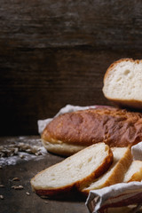 Homemade white wheat bread whole and slice served with wheat grain seeds and flour on white linen towel over dark wooden kitchen table. Rustic style.