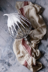 Process of cooking meringue. Whipped egg whites on mixer whisk on linen towel over gray texture background. Top view. Baking dessert concept