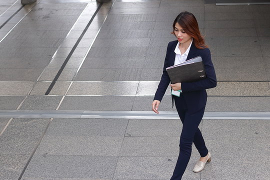 Aerial view of young attractive Asian business woman holding document folder and walking on flooring in the city against copy space background. - Powered by Adobe