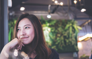 Closeup portrait image of a beautiful Asian woman with smiley face sitting in modern cafe with feeling good , beauty fashion and lifestyle with green vertical garden background