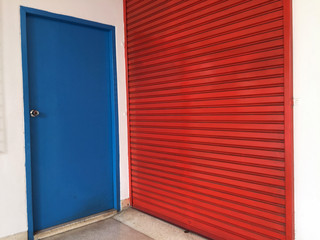 Two doors next to each other, Small blue wooden door for people to use,  big red metal door for Moving large stuff.
