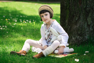 Little cute girl reading a book under big linden tree