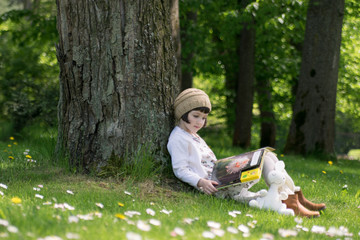 Little cute girl reading a book under big linden tree