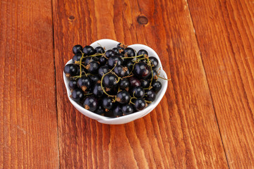 Black currants in ceramic bowl on wood background
