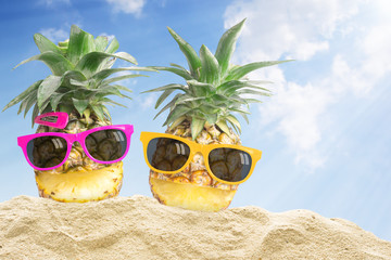 Fototapeta na wymiar Couple pineapple wearing sunglasses on beach. In summer holiday.