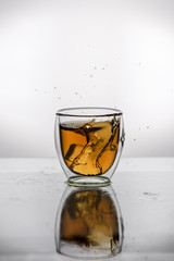 Splash of falling ice in a glass with tea