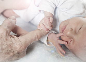 Little baby boy is holding his grandfather's hand