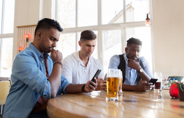 male friends with smartphone drinking beer at bar