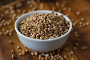 Buckwheat grain on ceramic bowl over wooden table.