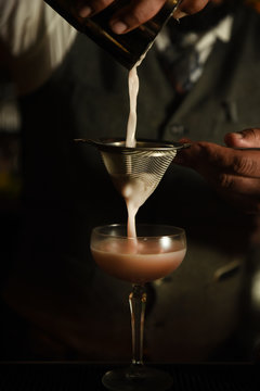 Bartender pouring a pink cocktail into a glass 