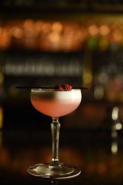 Glass of pink cocktail with raspberries on straw