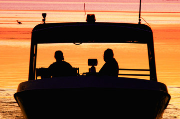 silhouette people on boat with sunset behind them 