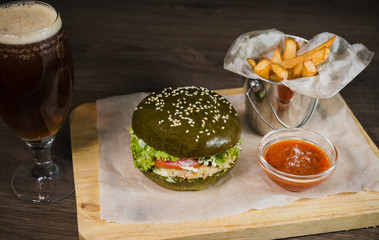 Green burger with fried potatoes and tomato sauce on a wooden stand with a glass of beer