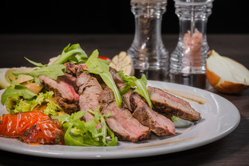 Roasted meat with blood in a cut with vegetables on a wooden background