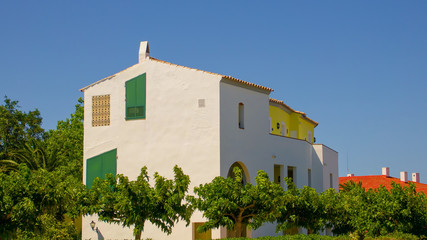 Houses on the island of Menorca in Spain with green shutters, yellow walls and yellow and orange tiled roofs.