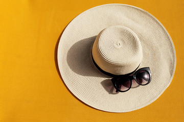 Beautiful straw hat with sunglasses on yellow vibrant vivid background. Top View. Summer Travel...