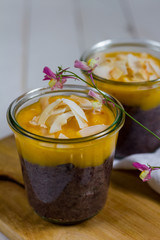 
Black rice pudding with mango and coconut flakes in the glass jar.  White background, wooden table.