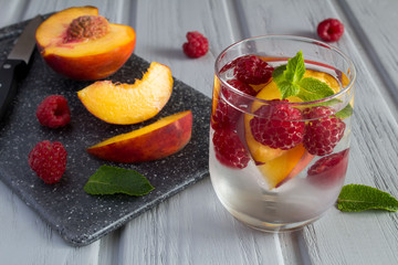 Detox water with raspberries and peach on the grey wooden background