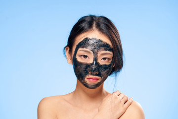 Beautiful young woman on a blue background in a black coal face mask, Asian