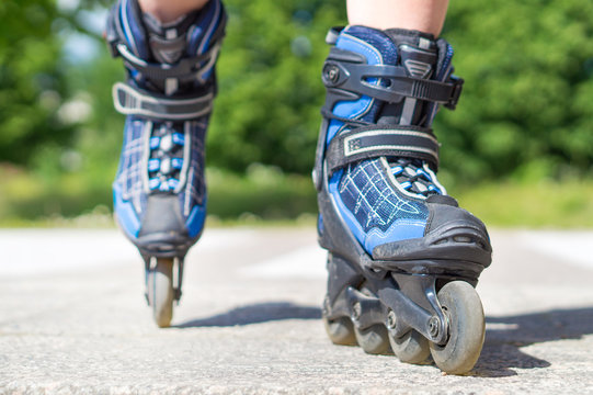 Roller skating in summer. Blue rollerskating on tarmac and asphalt on sunny day. Inline skating on asphalt in the city. Fun free time activity. Nature, trees and woods in the background.