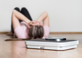 Weight loss fail concept. Scale and depressed, frustrated and sad woman lying on floor holding head...