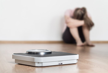 Weight loss fail concept. Scale and depressed, frustrated and sad woman sitting on floor holding...