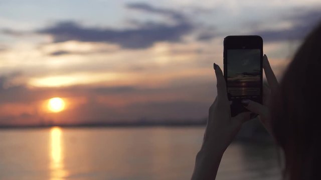 Girl takes photos of sunset on mobile phone camera