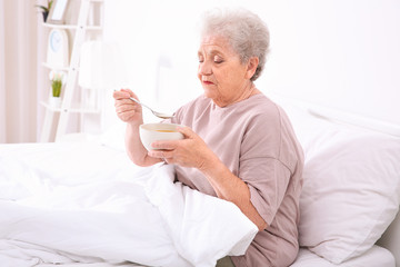 Elderly woman sitting in bed and eating soup
