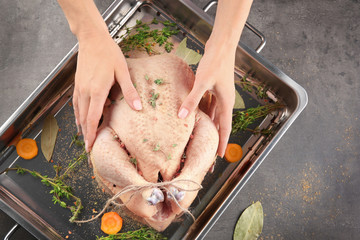 Woman cooking turkey with spices and herbs on baking sheet
