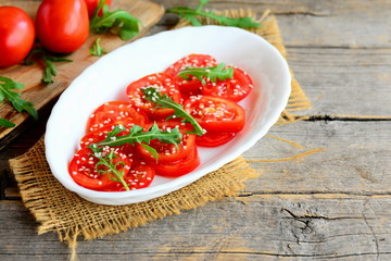 Light tomato and arugula salad. Delicious and dietary salad with tomatoes, arugula and sesame seeds on a white plate and a vintage wooden background with a copy empty space for text. Country style