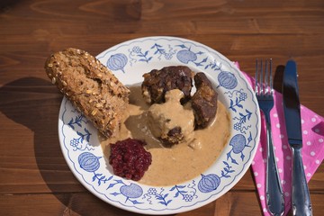 Slowly roasted roe deer venison with wild style creamy sauce served with rustic baguete and pickled cranberries on the old rustic plate. Very tasty traditional hunters dish in Europe or Czech Republic