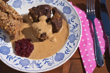 Slowly roasted roe deer venison with wild style creamy sauce served with rustic baguete and pickled cranberries on the old rustic plate. Very tasty traditional hunters dish in Europe or Czech Republic