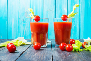 Tomato juice in glass with celery, cherry tomato on wood background