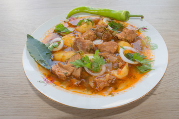 Tasty winter stew with meat and vegetables in bowl with ingredients over wooden table