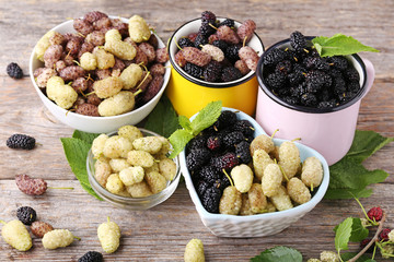 White, black and purple mulberries with mint leafs on wooden table