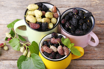 White, black and purple mulberries in mugs on wooden table