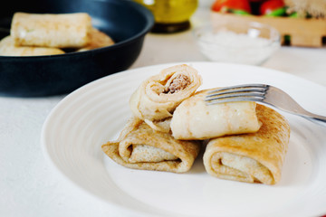Hearty and delicious breakfast or lunch, thin pancakes filled with chicken with fresh vegetables, herbs and olive oil on a light background