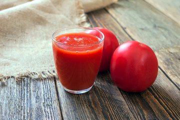 Tomato juice in a glass and two tomatoes on a wooden table