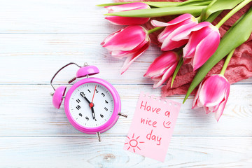 Bouquet of pink tulips with alarm clock and sheet of paper on wooden table